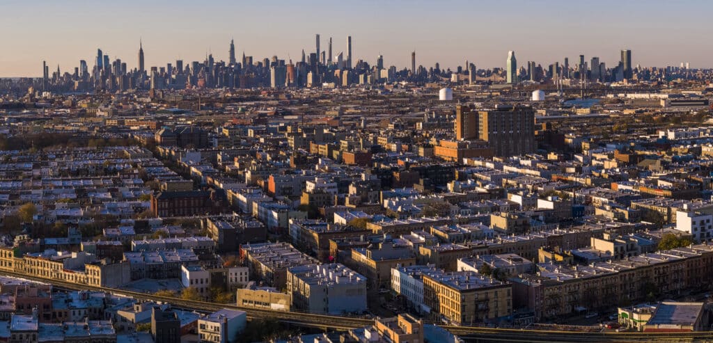 Remote view of the Manhattan Skyline illuminated in the night over the residential district of Bushwick, Brooklyn, in the sunset.
